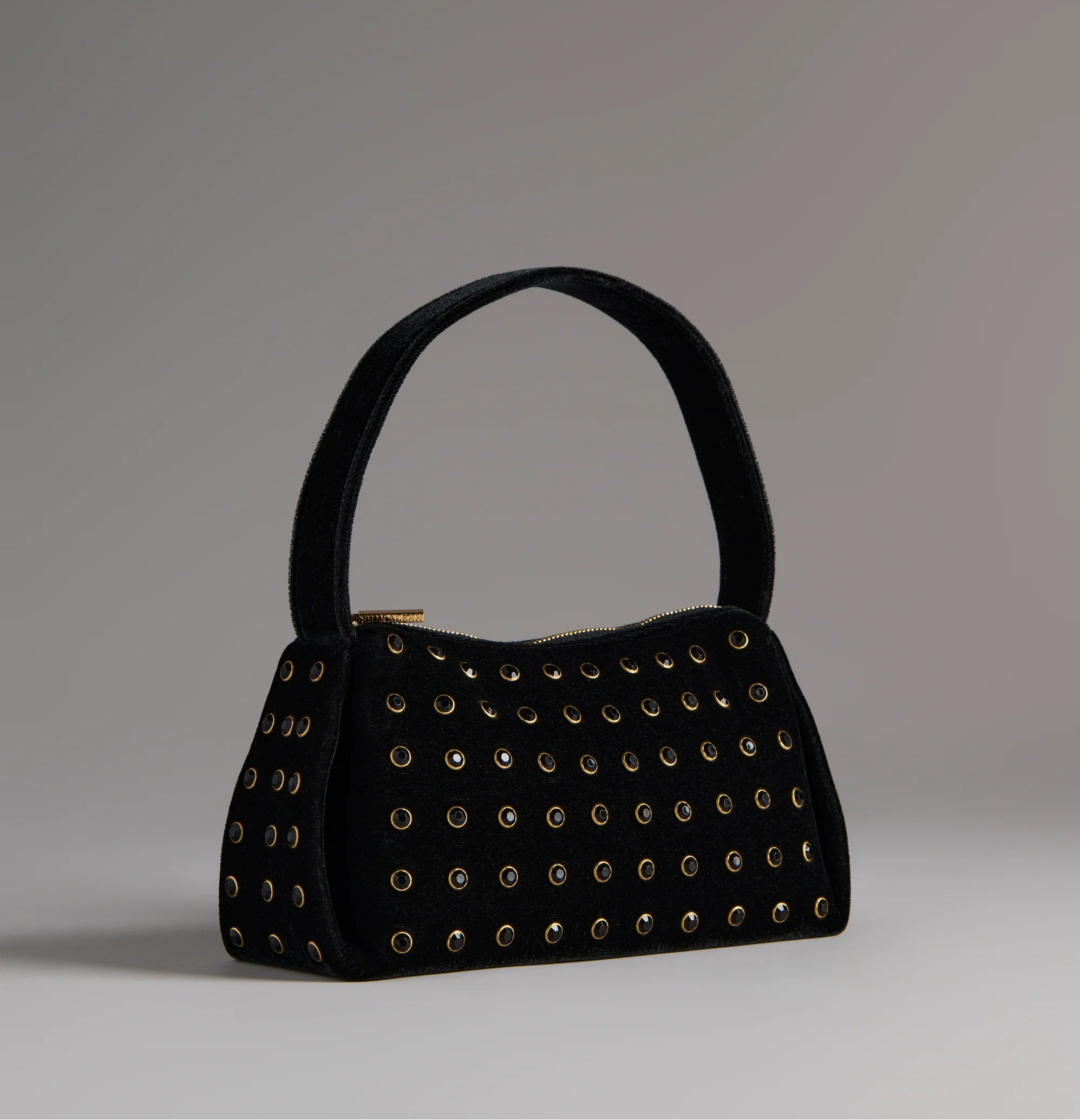Black handbag with gold studs on a gray background