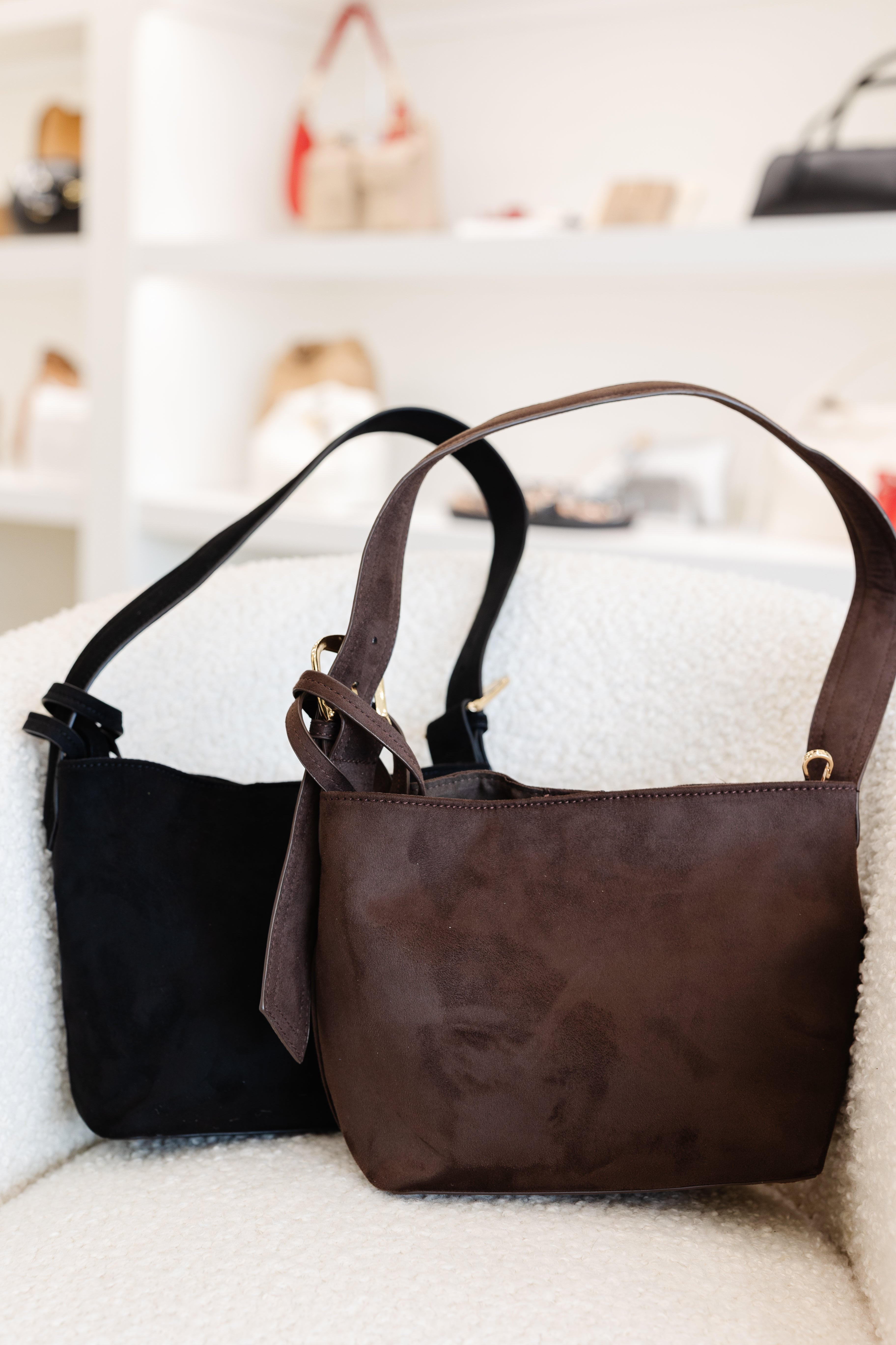 Two handbags, one black and one brown, on a white surface with a blurred background.
