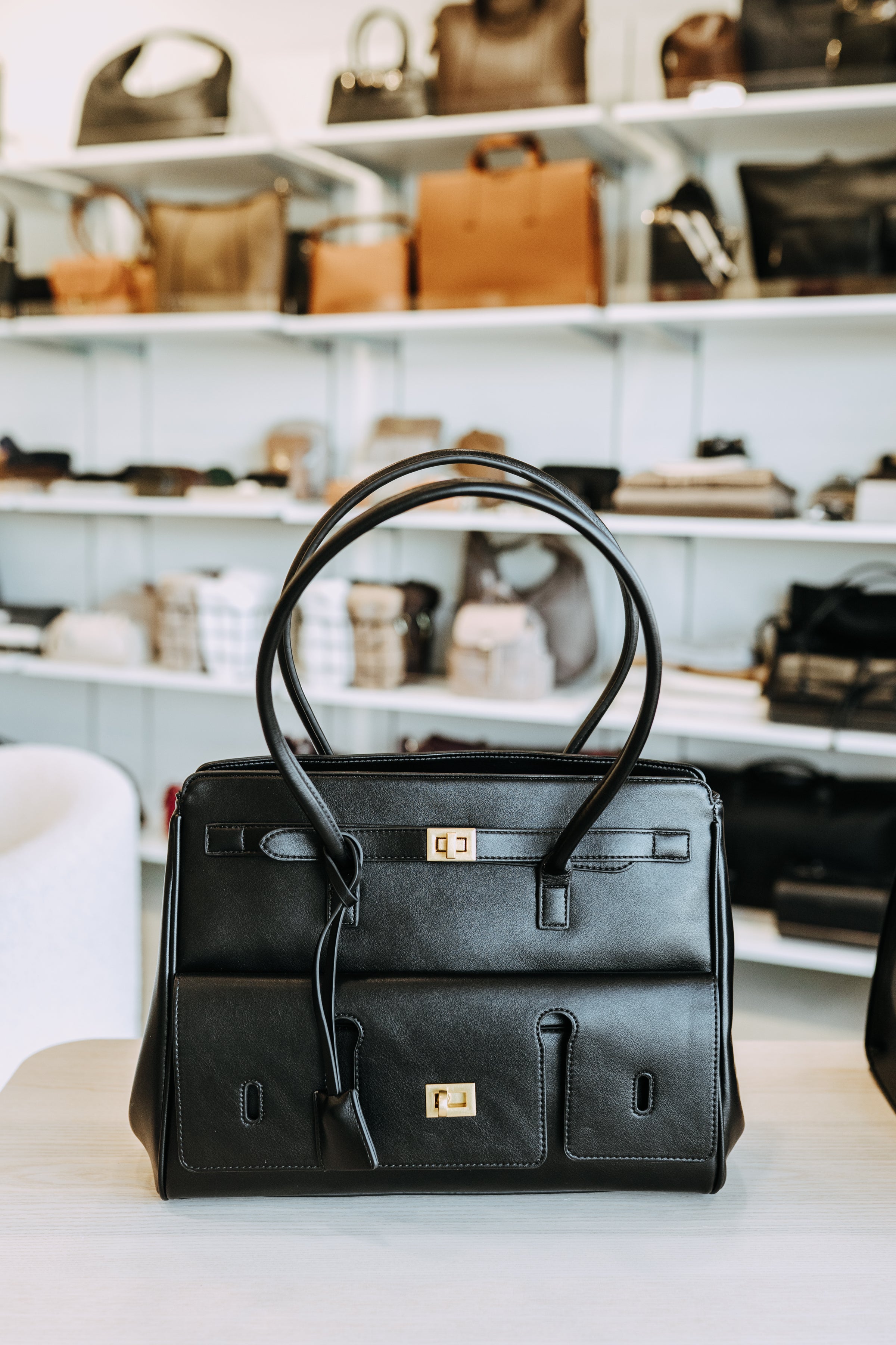 Black leather handbag on a table with shelves of bags in the background