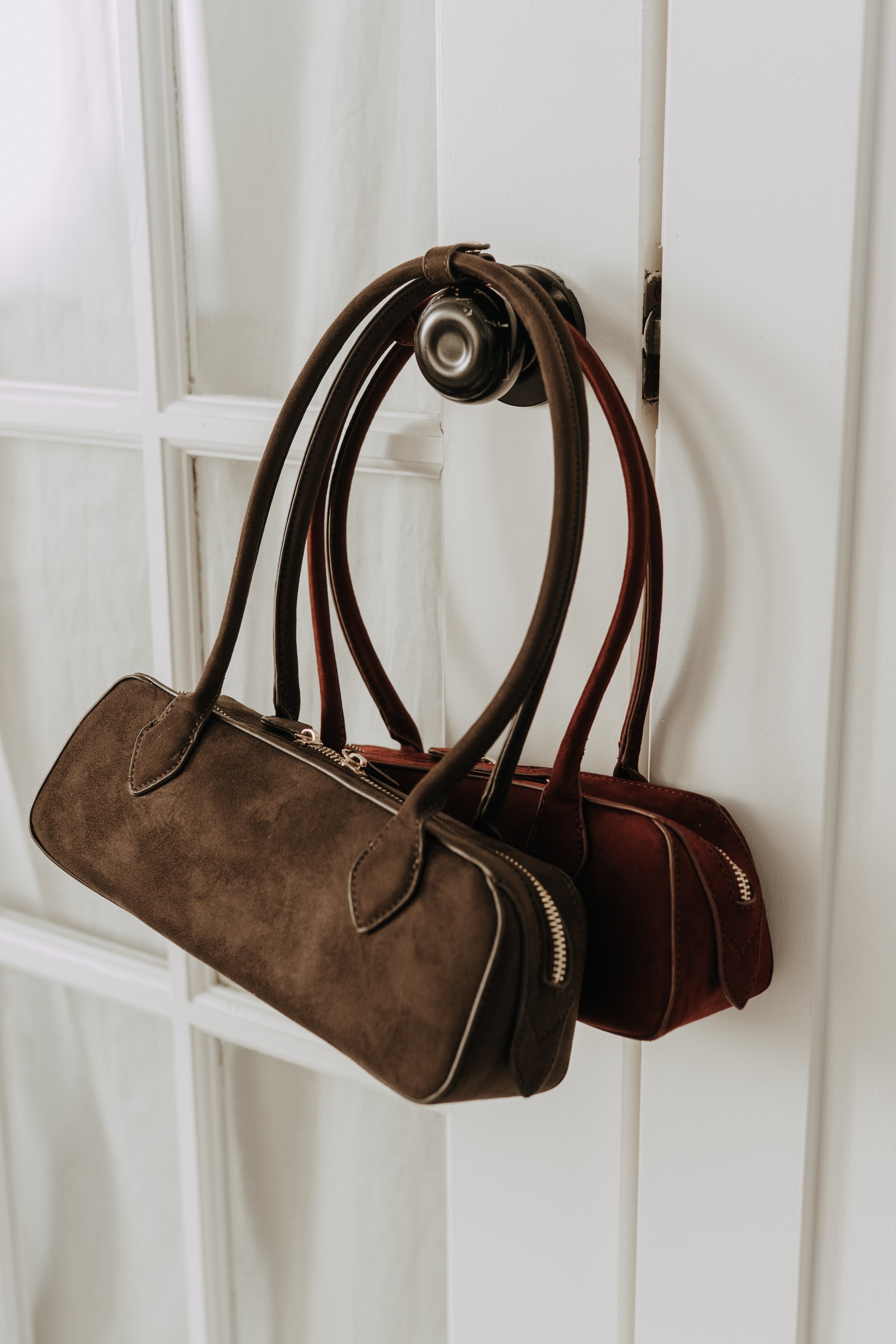 Brown handbag with black handles hanging on a white wall.